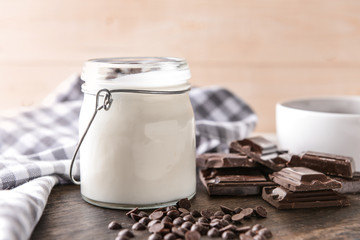 Jar with tasty yogurt and chocolate chips on wooden board