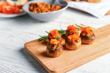 Wooden board with tasty stuffed mushrooms on white table