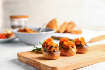 Wooden board with tasty stuffed mushrooms on white table
