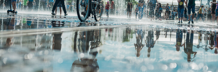 Reflection of the crowd of merry people in the city fountain, in the pool. Bright sunny spring or...