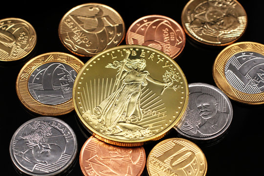 A macro image of miscellaneous Brazilian coins with a American one ounce gold panda coin on a black reflective background close up 