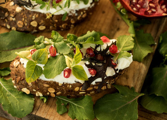 bauernbrot belegt mit frischkäse, verschiedener sorten rucola und granatapfelkernen