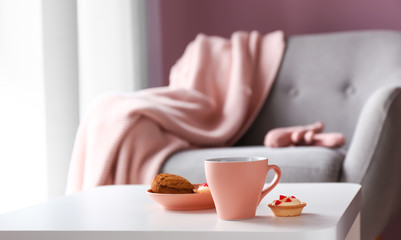 Cup of hot tea and sweets on table in room