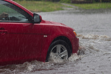 Red car rides in heavy rain on a flooded road