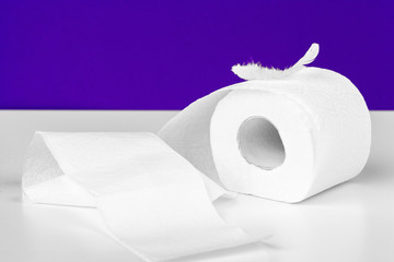 Roll of toilet paper and soft feather on color table