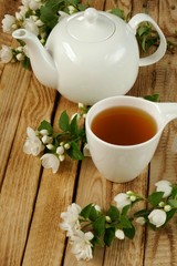 Jasmine tea. bio tea with jasmine extract, white teapot and white mug with tea, blooming sprigs of jasmine on a wooden brown background.Herbal organic wholesome tea