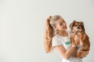 Young female volunteer with dog on light background