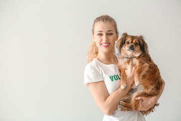 Young female volunteer with dog on light background