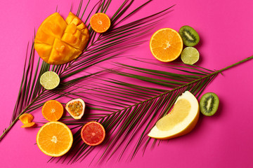 Assortment of tasty exotic fruits with palm leaves on color background