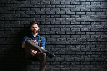 Fototapeta na wymiar Fashionable young man sitting near dark brick wall