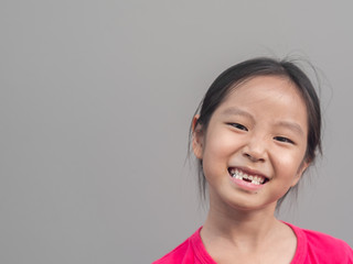 Asian little cute girl smile with her broken tooth , grey background