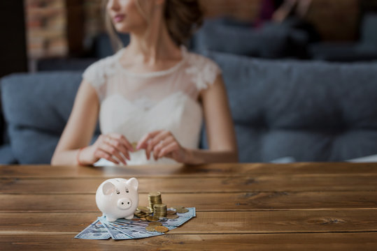 The bride puts  money in piggy box. Closeup coins and dollars near moneybox
