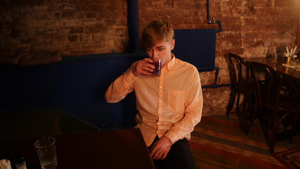 A man in shirt sitting in the bar by the table and drinking