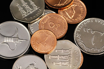 A macro image of assorted coins from the United Arab Emirates on a reflective black background