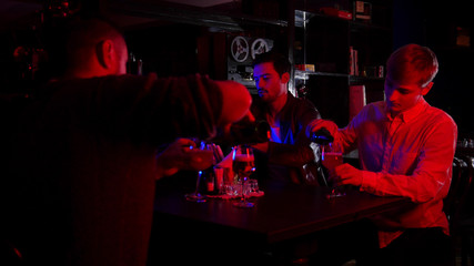 Bar with neon lighting. Group of friends sitting by the table and pouring beer in the glasses