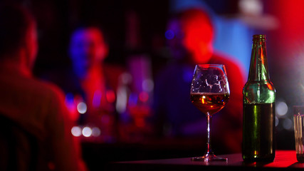 Bar with neon lighting. A bottle and glass of beer standing on a table.