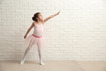 Cute little ballerina near white brick wall