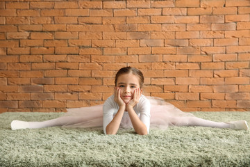 Cute little ballerina stretching near brick wall