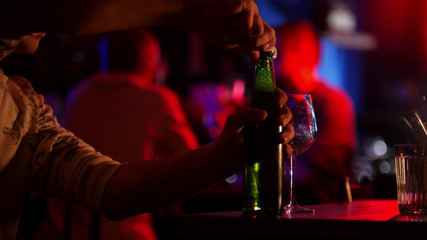 Bar with neon lighting. A man opens up a beer bottle