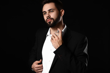 Handsome man with bottle of perfume on dark background