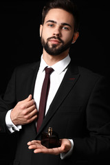Handsome man with bottle of perfume on dark background