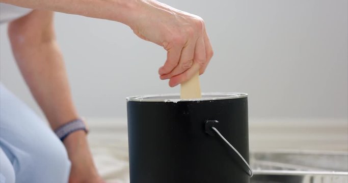 Woman stiring paint can with paint stick before painting room - slow motion - close up