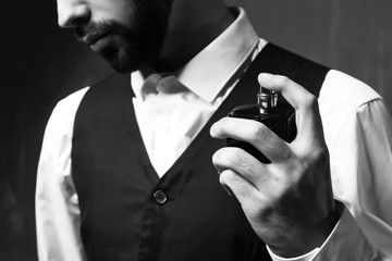 Handsome man with bottle of perfume on grey background, closeup
