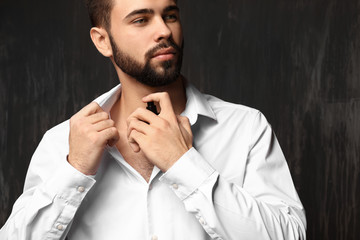 Handsome man with bottle of perfume on grey background