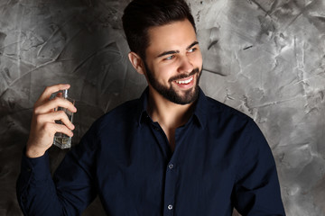 Handsome man with bottle of perfume on grey background