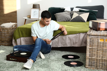 Young man listening to music on record player at home