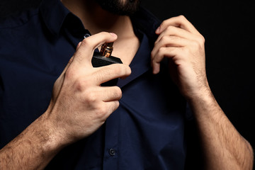 Handsome man with bottle of perfume on dark background, closeup