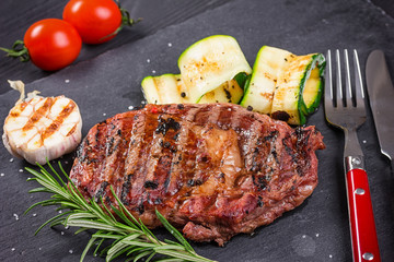 Juicy medium rare beef steak slices on ceramic board with herbs spices and salt.