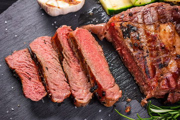 Juicy medium rare beef steak slices on ceramic board with herbs spices and salt.