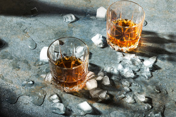 Celebrating at the bar. Pair of glasses with whisky and pieces of ice on gray table