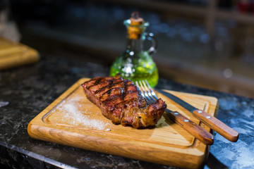 Juicy medium Beef Rib Eye steak on wooden board with fork and knife herbs spices and salt.