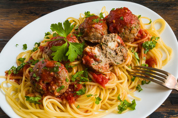 Pasta and meatballs with mozzarella inside, tomato sauce, fresh parsley on white plate, close-up