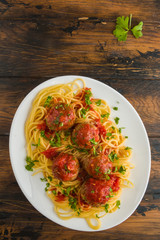 Pasta and meatballs with mozzarella, tomato sauce, fresh parsley, white plate on wooden rustic table, top view