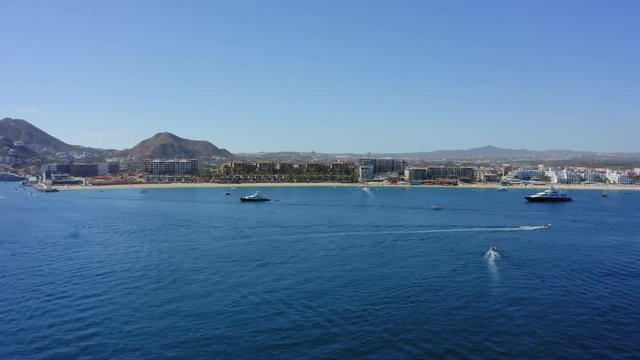 An aerial shot flying over boats towards the beach and resorts in Cabo San Lucas