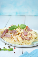 Pasta carbonara with basil on a plate, standing on a wooden white table, next to a blue towel