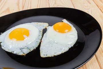 Fried eggs prepared sunny side up on black dish closeup