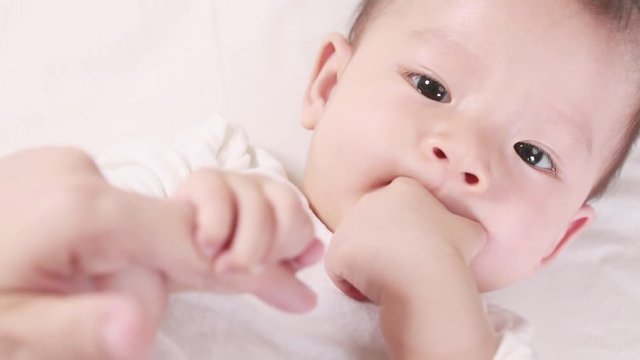 Cute asian baby sucks the thumb and lying on the bed with her mom, New family and baby healthy concept
