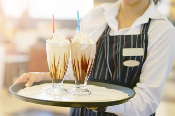 Waitress bears two vanilla milkshakes for the client of the hotel restaurant. Two chocolate dairy cocktails on a waitress tray. Toning.