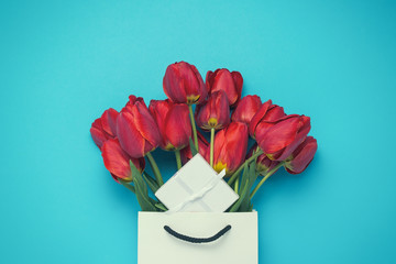 White Gift Bag, a small white gift box and a bouquet of red tulips on a blue background. Concept Offers an engagement or marriage, shopping
