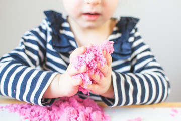 Obraz na płótnie Canvas Little Happy Caucasian Girl Playing with Pink Kinetic Sand at Home Early Education Preparing for School Development Children Game