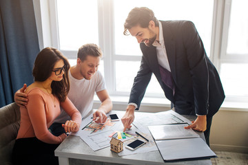 Couple buy or rent apartment together. They sit in front of realtor and choose apartment plan. Young man in suit point on it. Helpful and concentrated.