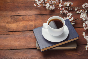 Sakura branches with flowers, White cup with Black Coffee and two books on a dark wooden background. Concept of Spring