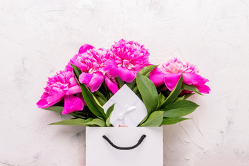 Peony bouquet in white bag and gift box on white background.