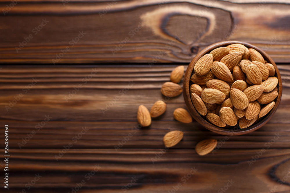 Wall mural Delicious almonds in a wooden bowl on a wooden table, view from above