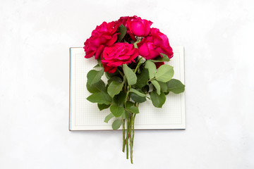 Bouquet of red roses on an open diary on a light stone background. Flat lay, top view
