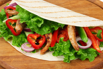 Tortilla wrap with fried chicken meat and vegetables on wooden board isolated on white background